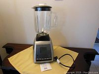 Full view of Black & Decker blender with glass jug, black lid, sitting on yellow cloth with power cord coiled alongside.