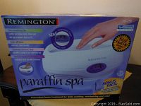 Box of Remington Paraffin Spa HX-290 with hand on device, highlighting branding, bonus pack and features.