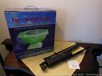 Boxed Fog Design Lamp showing product packaging and two black foldable music stands on table.