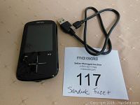 Front view of the black SanDisk Sansa Fuze+ MP3 player with USB cable alongside a MaxSold auction info card.