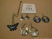 Photo showing four pairs of earrings and a butterfly pendant necklace on chain laid out on a beige cloth.