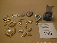 Lot of 11 assorted costume brooches including sailboat, bird, floral cameo, pearl cluster, monkey, bow, starfish, heart with pearl, rhinestone cluster, butterfly in box, and small shoe.