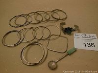 All bangles and bracelets arranged on a beige cloth next to the decorative silver spoon with green stone handle and Aztec calendar bowl engraving.