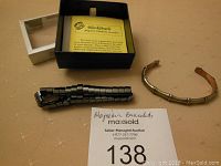 Two men's magnetic bracelets displayed on a beige surface, one black segmented bracelet and one bronze-tone bamboo-style cuff, box with BlackGuard label in background.