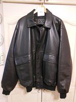 Front view of men's black faux leather bomber jacket hanging on a wooden hanger.