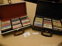 Two carry cases shown open on a table, each filled with cassette tapes in rows.