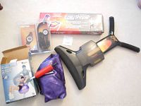 Assortment of exercise items including Tony Little Easy Shaper in box, purple exercise ball partially inflated, red hand pump, and packaged heart rate monitor on floor.