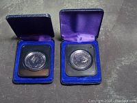 Two uncirculated 1975 Royal Canadian Mint silver dollars displayed in blue velvet presentation cases with purple satin interiors, coins in protective plastic holders
