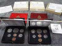 Top-down view of four uncirculated coin sets in red leather cases and associated original boxes and informational pamphlets showing years 1973 and 1975 clearly.