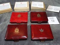 Four red leather or leatherette Canadian Mint coin cases and their original boxes and informational inserts arranged on a surface.