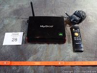 MyGica Ultra HD 4K Android TV Box with external antenna, remote control, and power adapter shown next to an orange ruler for scale.
