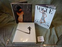 View of two hardcover coffee table books and clear protective plastic case laid out on fabric surface.