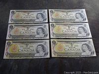 Front sides of six Canadian one dollar bills from 1973 with Queen Elizabeth II portrait visible.