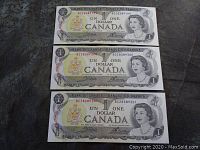 Front view of three consecutive Canadian one dollar bills from 1973 showing the portrait of Queen Elizabeth II, serial numbers and Bank of Canada markings.