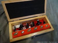 Open wooden box displaying 6 router bits in foam insert with labeled bit types on an orange card inside box.