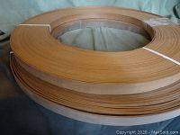 Photo showing two large coils of wood edge banding strips, light brown and reddish in color, rolled and bound for sale.