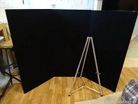 Black modular four-panel display stand set up on wooden floor, connected with hinges.
