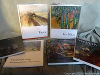 Photo showing six art books arranged on a cloth surface featuring Turner, Van Gogh, Monet, Vermeer, Rodin, and another Van Gogh book.