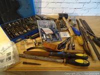 Wide view of entire assortment showing drill bits, mallet, files, rasps, and hand tools arranged on wooden table