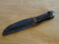 Bowie knife inside black leather sheath showing full length of sheath and handle.