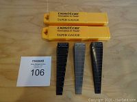 Photo showing all three taper gauges laid out on wooden surface with two yellow plastic protective cases above them and lot number card.