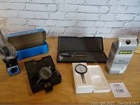 Measurement tools arranged on wooden table: digital caliper in black case, dial indicator in foam, magnetic base in box, Crotex dial indicator box.