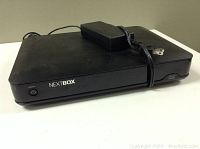 Front and top view of black Cisco NextBox digital video converter with power adapter and power cord on top.