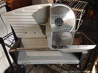 Photo of Waring Pro food slicer from side showing blade, food holder, and slicing tray, with visible residue and signs of use.