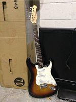 Full front view of the Stagg sunburst electric guitar leaning against a box
