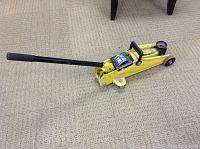 Yellow 2 ton trolley jack on beige carpet with black handle extended.