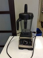 Full view of blender assembly including base, container, tamper and power cord on table surface