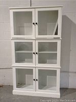 Front view of the white cabinet showing the three stacked sections with glass doors and shelves