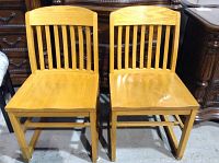 Front view of two wooden chairs side by side showing light wood finish and vertical slats on backrest.