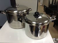 Two large stainless steel pots with lids on a white surface.