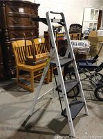 Single three-step painter's ladder standing open on a warehouse floor with visible non-slip steps and a top black tool tray
