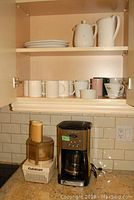 Photo of Cuisinart food processor and coffee maker with ceramic mugs and dishes on shelf above