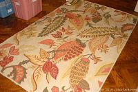 Full view of the custom made designer rug with floral and leaf patterns in warm colors laid on hardwood floor.