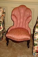 Front view of pink upholstered antique slipper chair with scalloped shell-like back and floral patterned fabric
