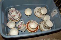 Plastic bin containing multiple tea cups with matching saucers all stacked inside, showing various floral patterns and gold rims.