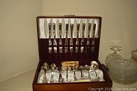 Open wooden chest displaying 8 place settings of knives in the upper compartment and assorted spoons in the lower compartment with a Community label.