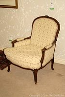 Front angle view of the occasional chair showing the carved wood frame and patterned beige upholstery with armrests.