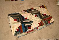 Folded quilt with multi-colored patchwork squares on carpet.