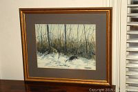 Framed watercolour painting showing a winter woodland scene with birch trees and snow, visible in a gold frame with gray matting.