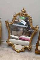 Image showing the full mirror with ornate gold painted carved frame and irregular shape, size marked as 24x34 inches.