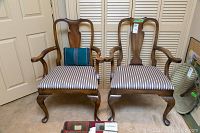 Front view of the two wooden armchairs with upholstered seats with stripes and a blue Christmas pillow on one chair.