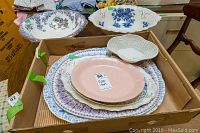 Box containing multiple platters and dishes of various sizes, designs and colors including pink and blue floral patterns.