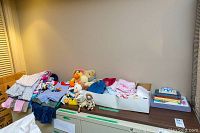 Assorted baby clothing, hats, stuffed animals and dolls arranged on a table