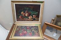 Two framed paintings stacked, one featuring peaches and grapes, the other apples on branches.