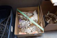 Box with broken glass chandelier components including hanging prisms and bulbs, resting inside a cardboard box.