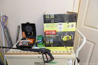 Ryobi pressure washer box, toolbox with Black & Decker drill, wooden yardstick, and meter stick laid out on cabinet.